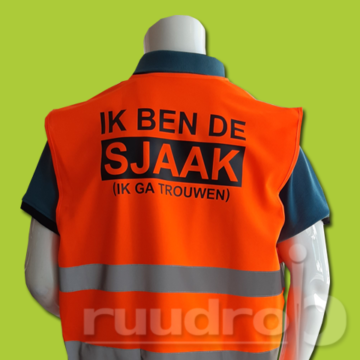 Een oranje veiligheidsvestje bedrukt met de tekst IK BEN DE SJAAK IK GA TROUWEN